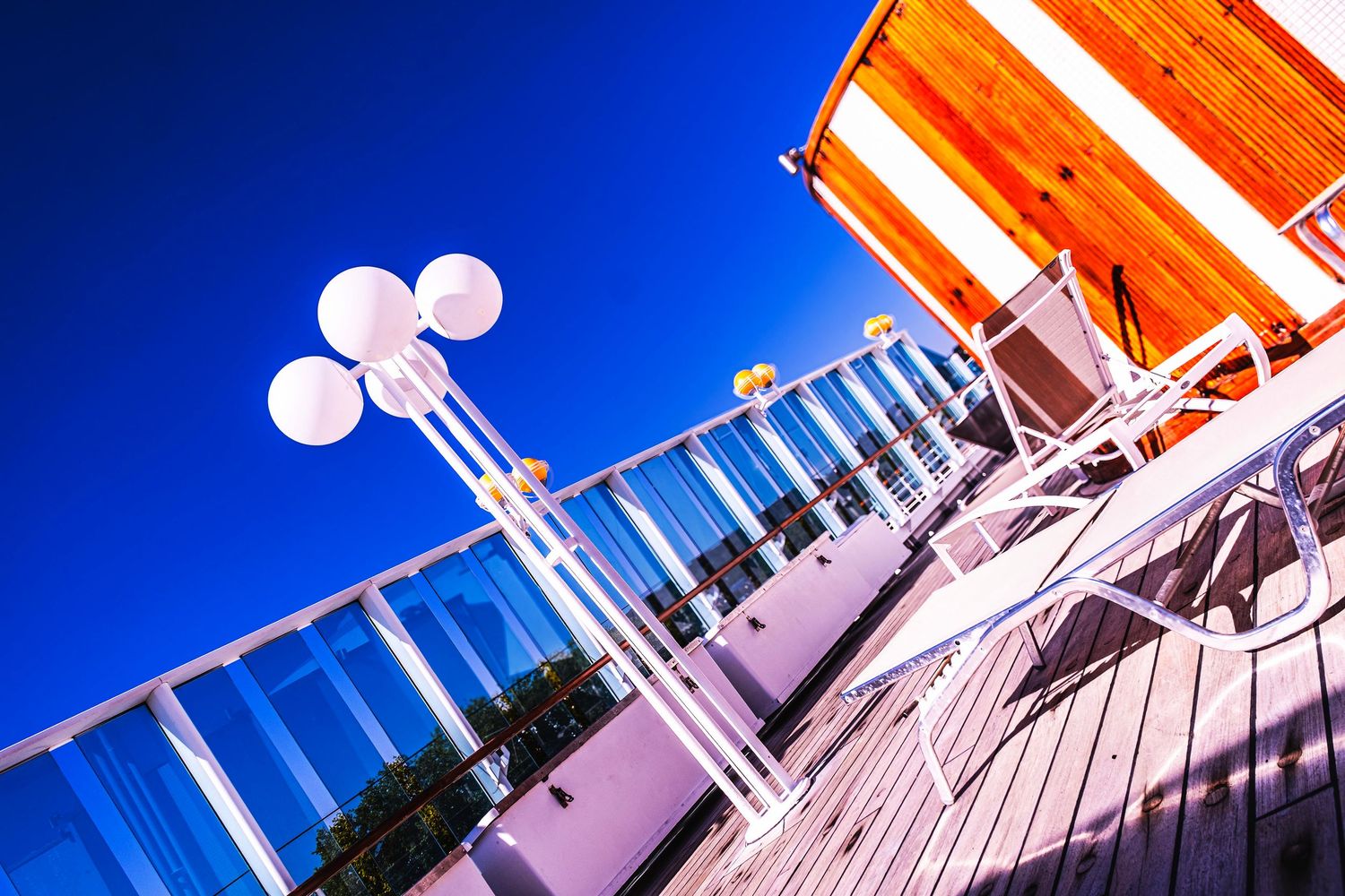 Outdoor rooftop terrace with white balloon lights, chairs, and orange striped awning under a vivid blue sky.