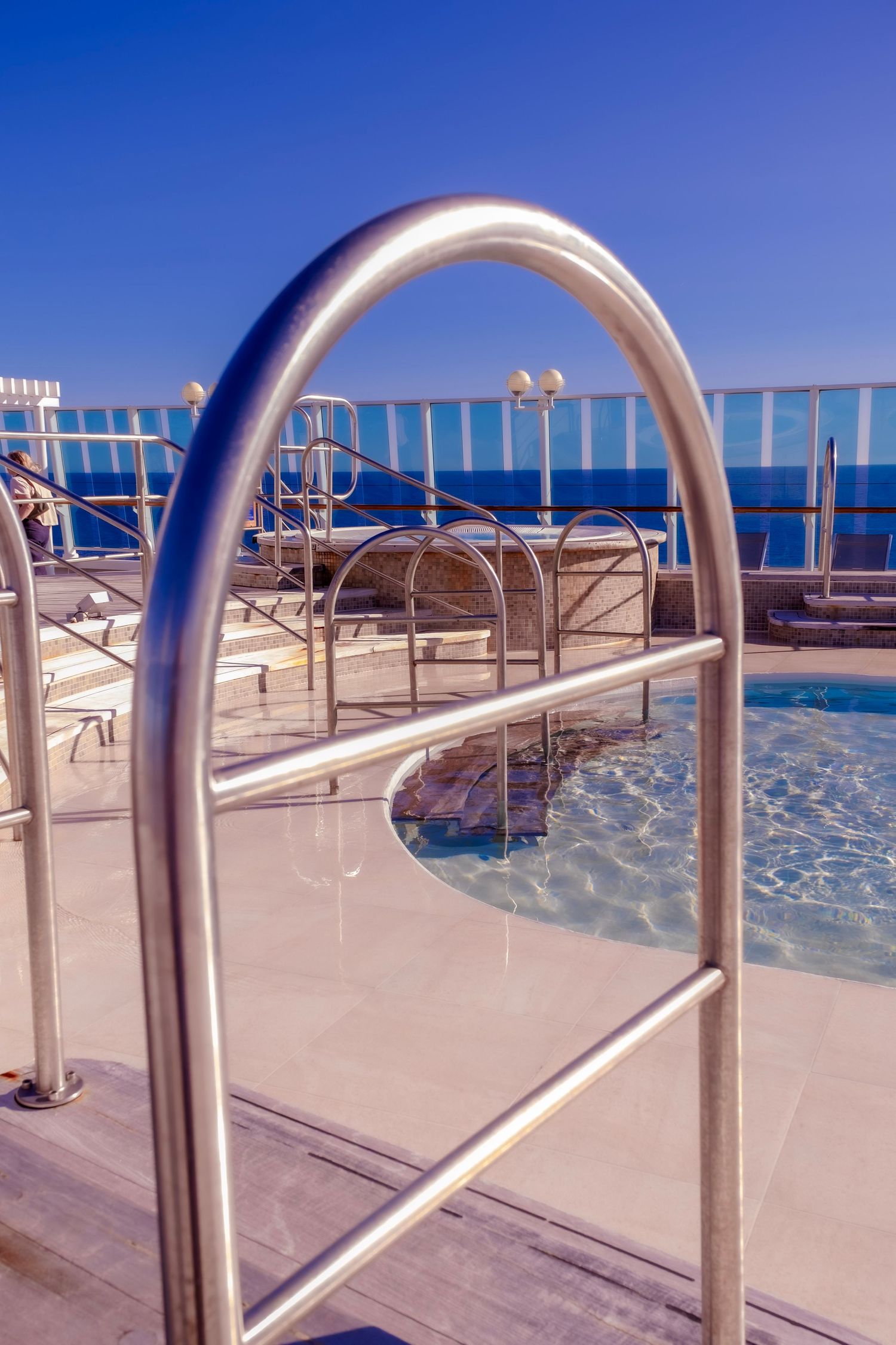 Stainless steel pool handrails beside a shimmering outdoor swimming pool with ocean views under a clear blue sky.