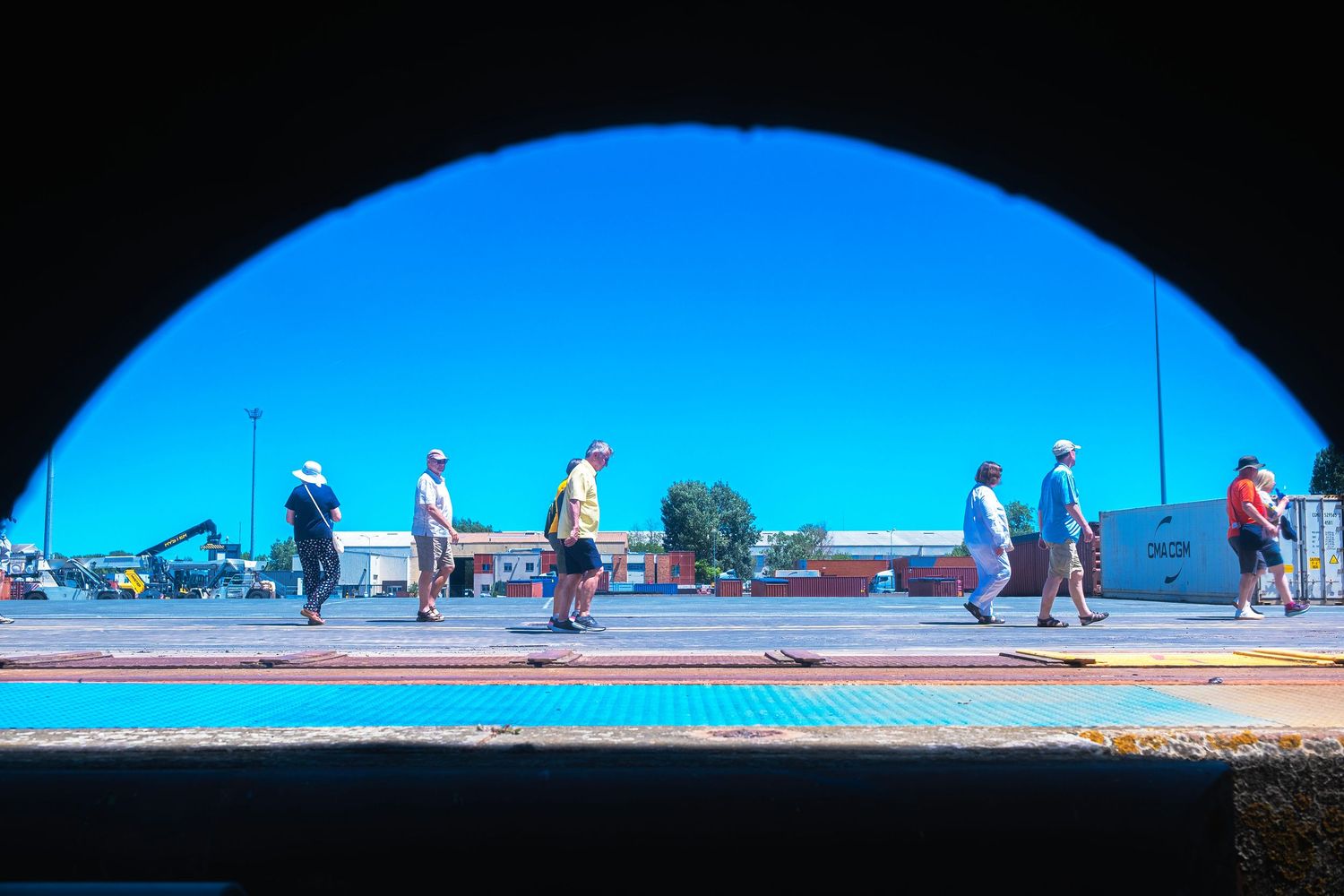 People walking outdoors viewed through an arch tunnel framing a bright blue sky and colorful street scene.