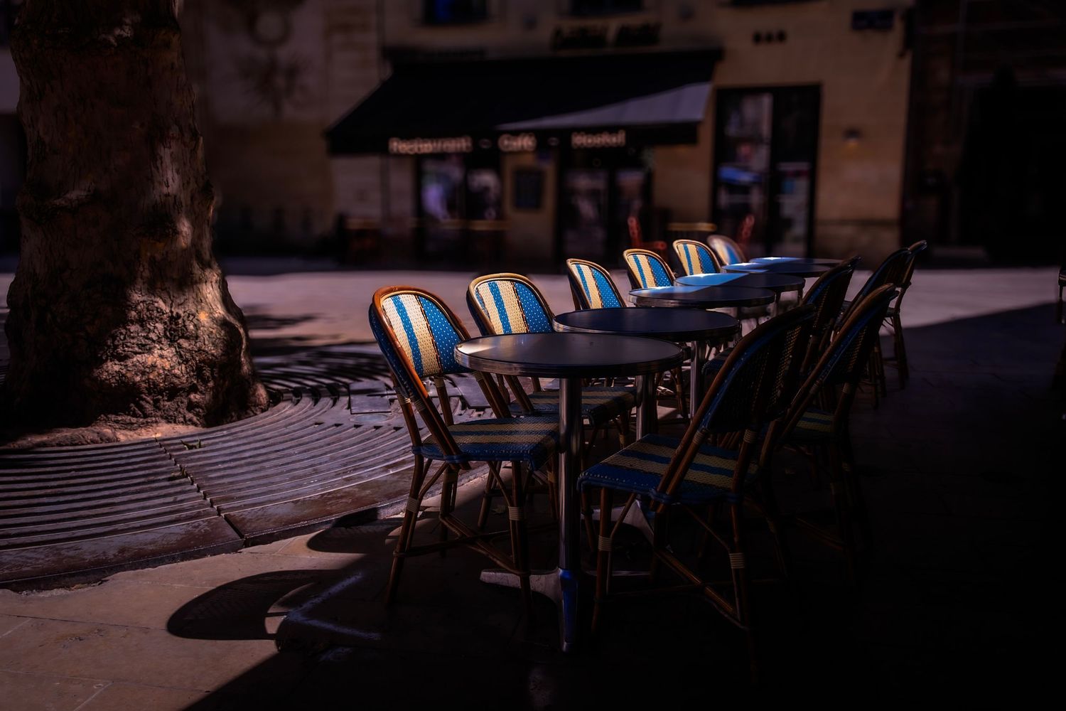 Empty bistro chairs and tables on a dimly lit Parisian outdoor cafe terrace at night.