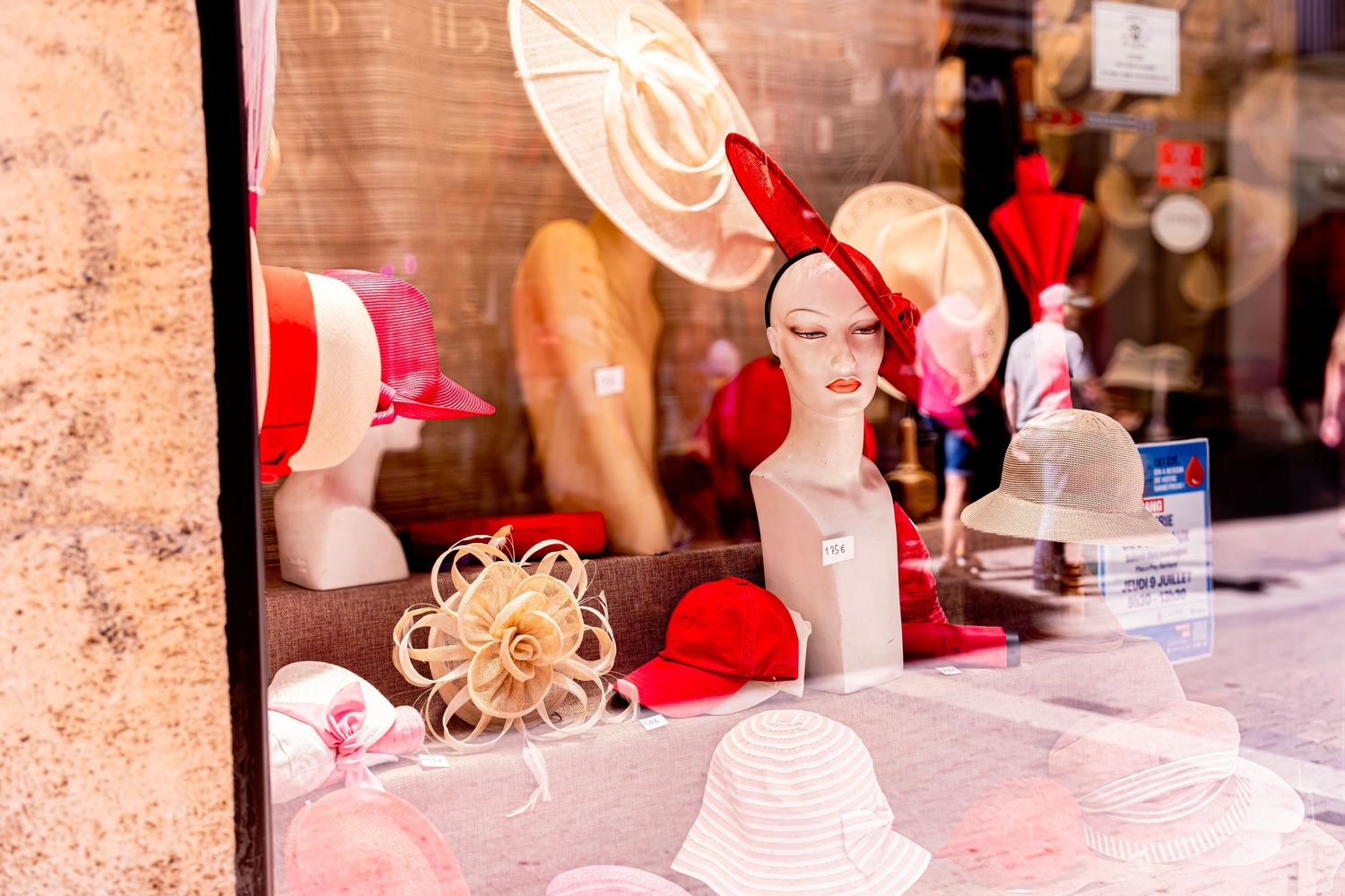 Colorful hat shop window display with mannequin heads wearing red and white hats in an elegant boutique.