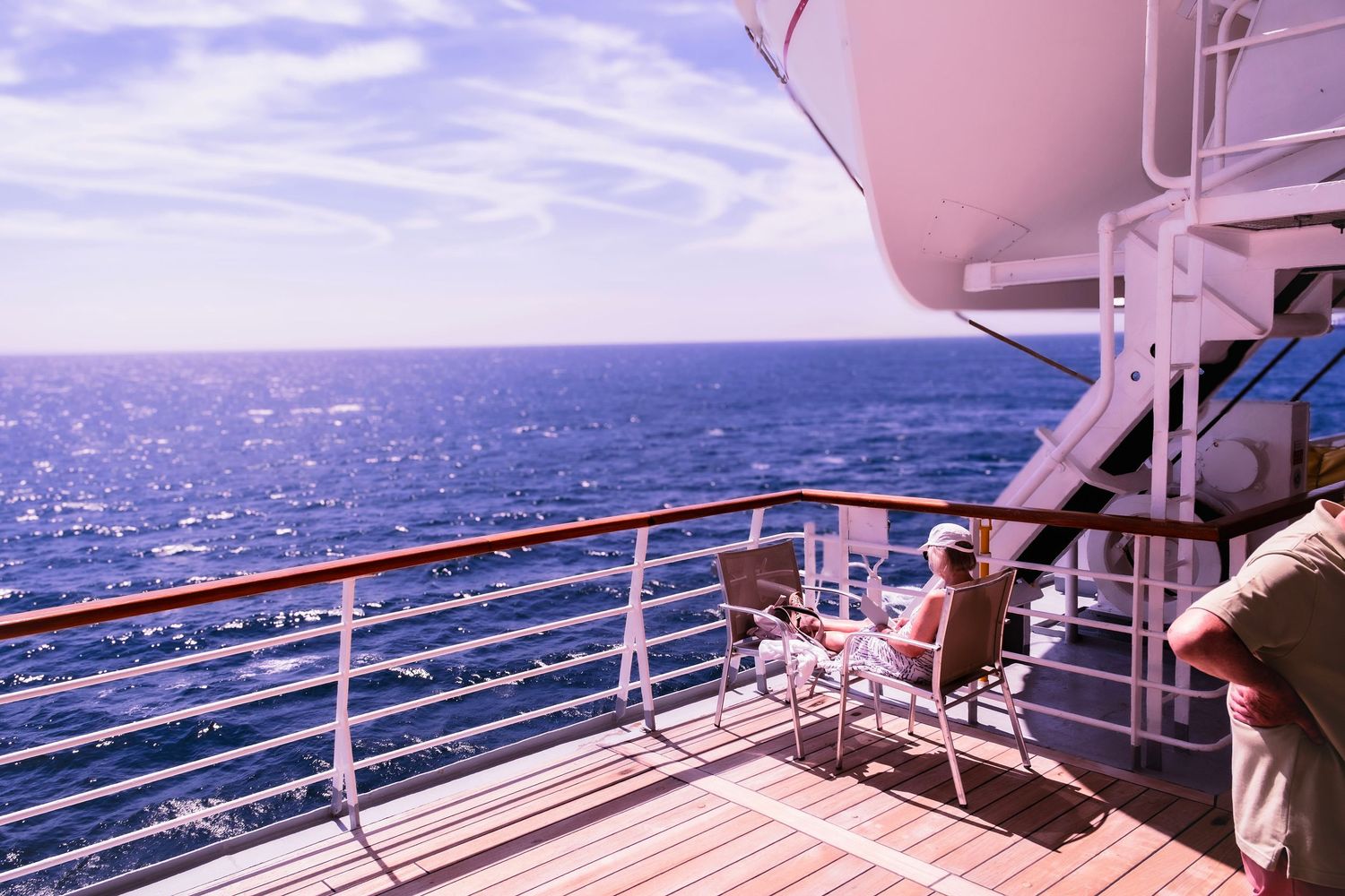 Sunny cruise ship deck with lounge chairs overlooking a sparkling blue ocean horizon.