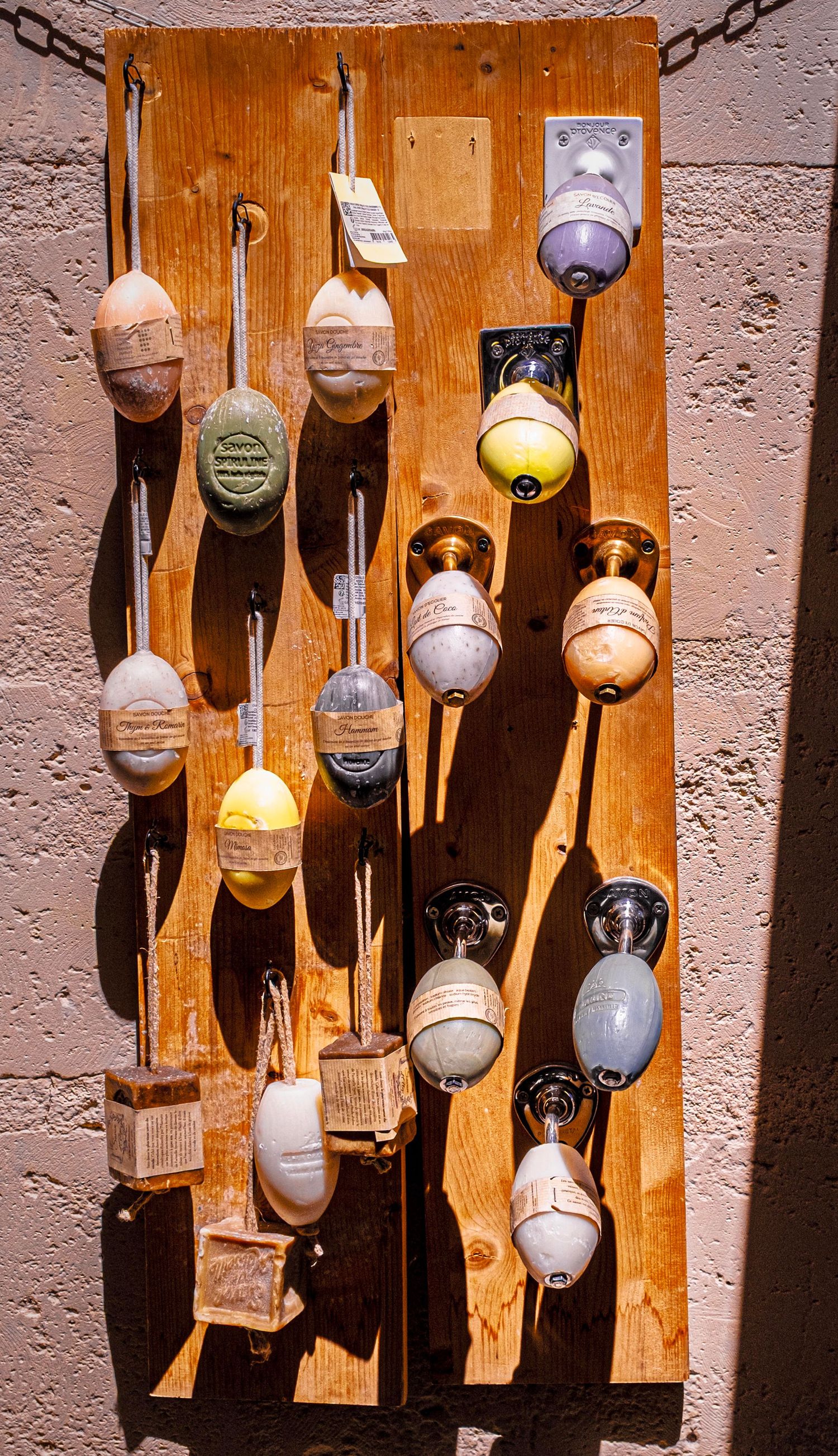Vintage fishing buoys and floats displayed on a rustic wooden board mounted on a textured wall in bright sunlight.