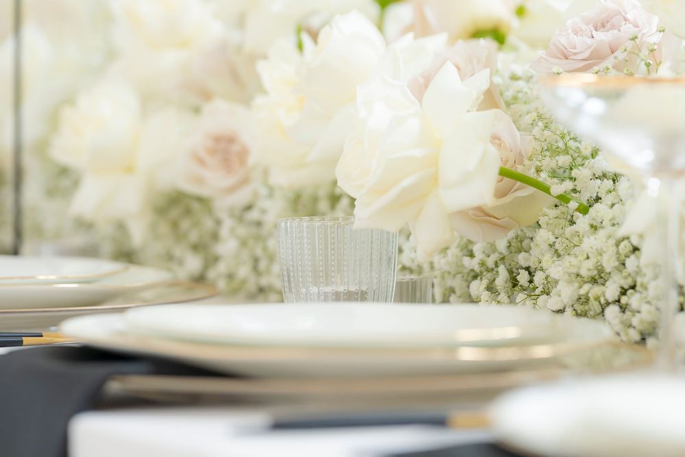 Delicate white floral arrangements with roses and baby's breath on reception table.