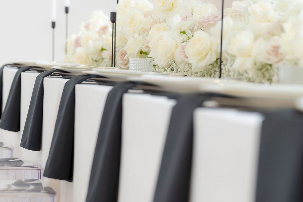Modern wedding reception table settings with white floral centerpieces and black chairs.