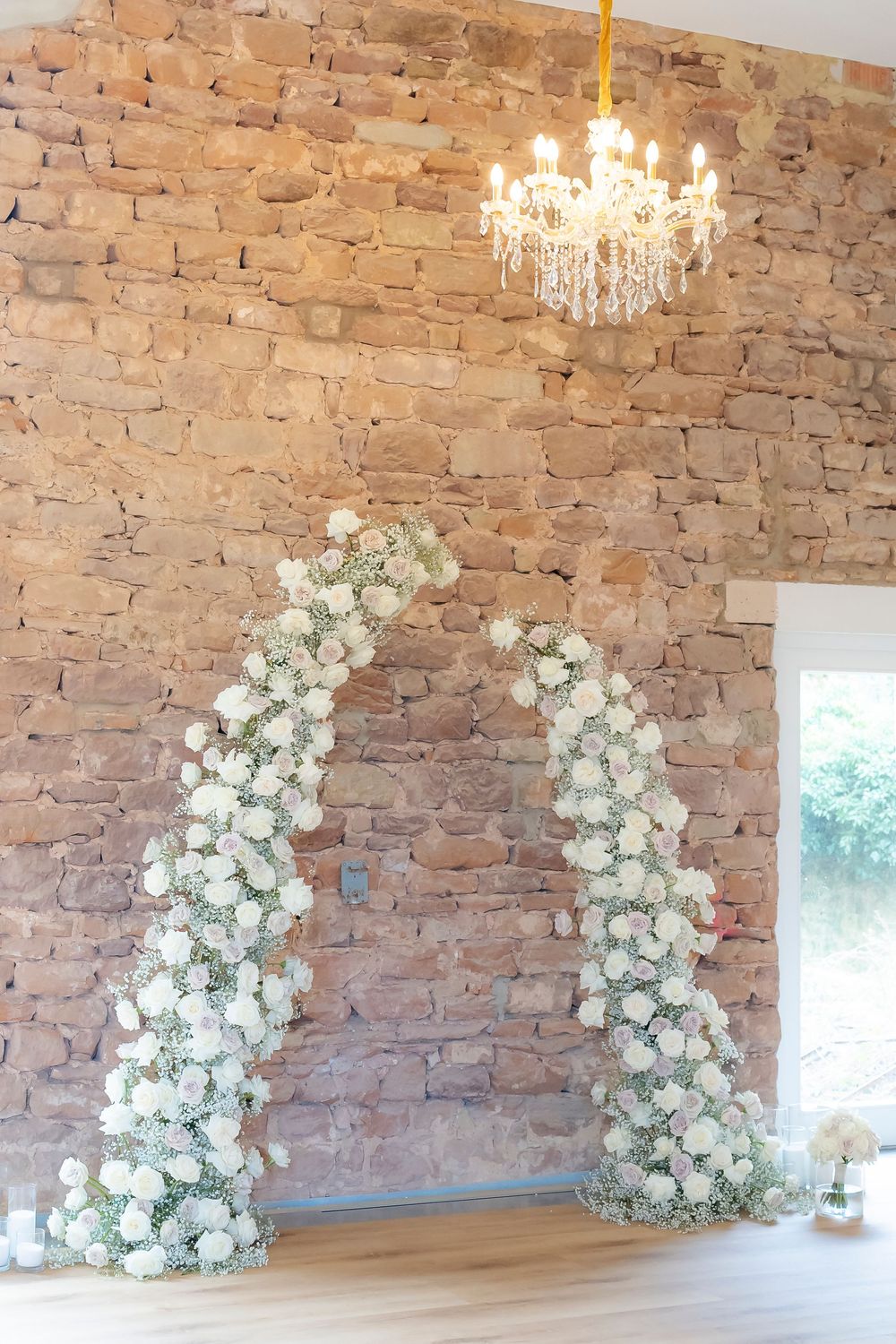 Rustic brick wall decorated with cascading white floral arrangements and crystal chandeliers.