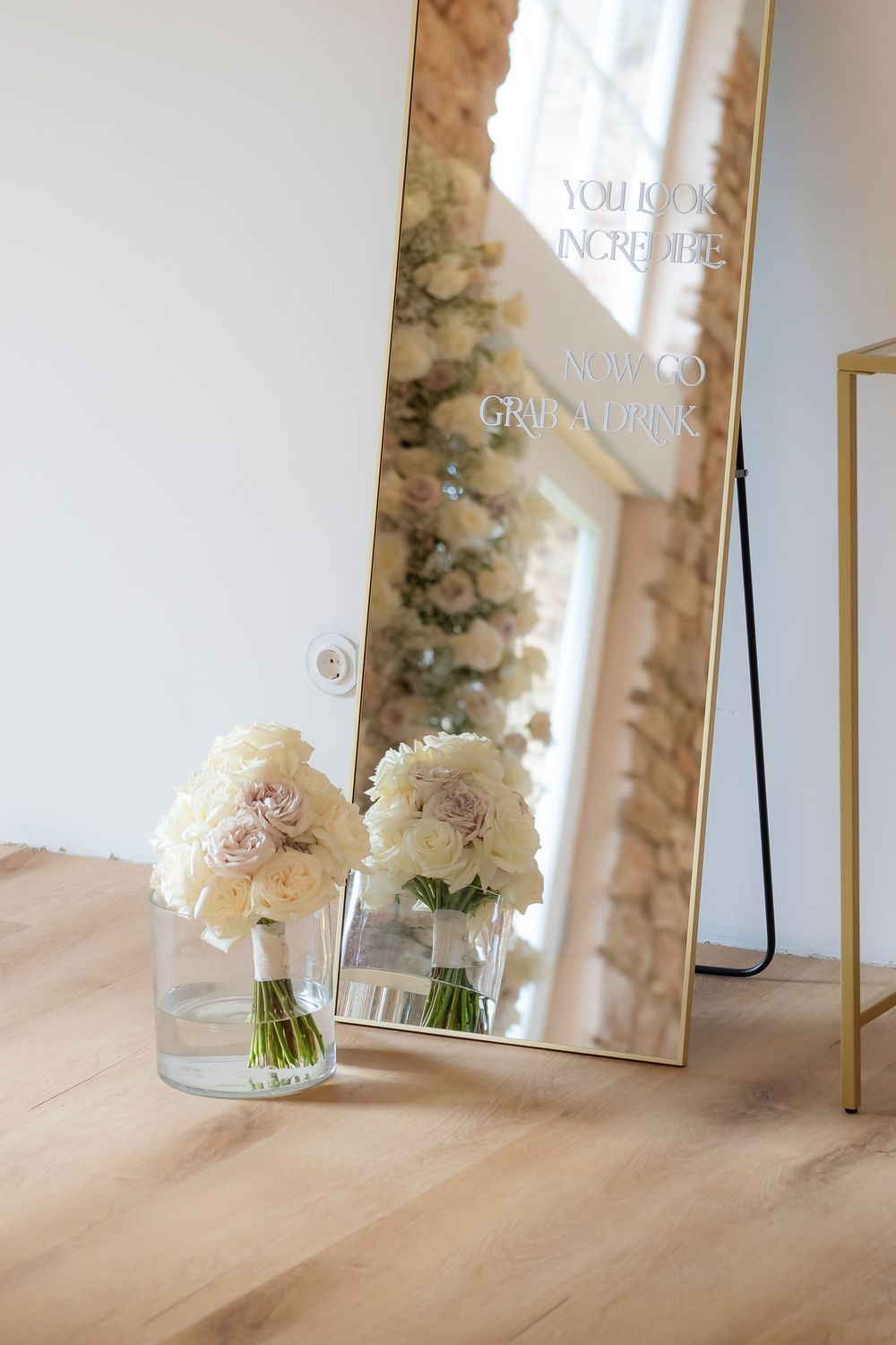 Wedding signage and white floral arrangements reflected in a gold-framed mirror.