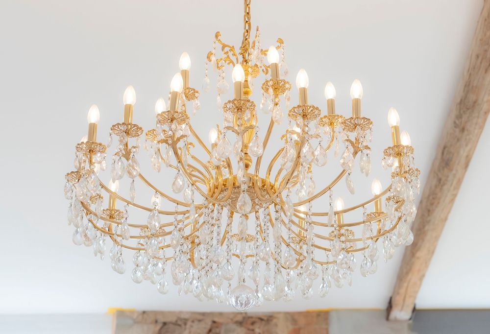 Elegant gold crystal chandeliers hanging from a white ceiling in an event venue.