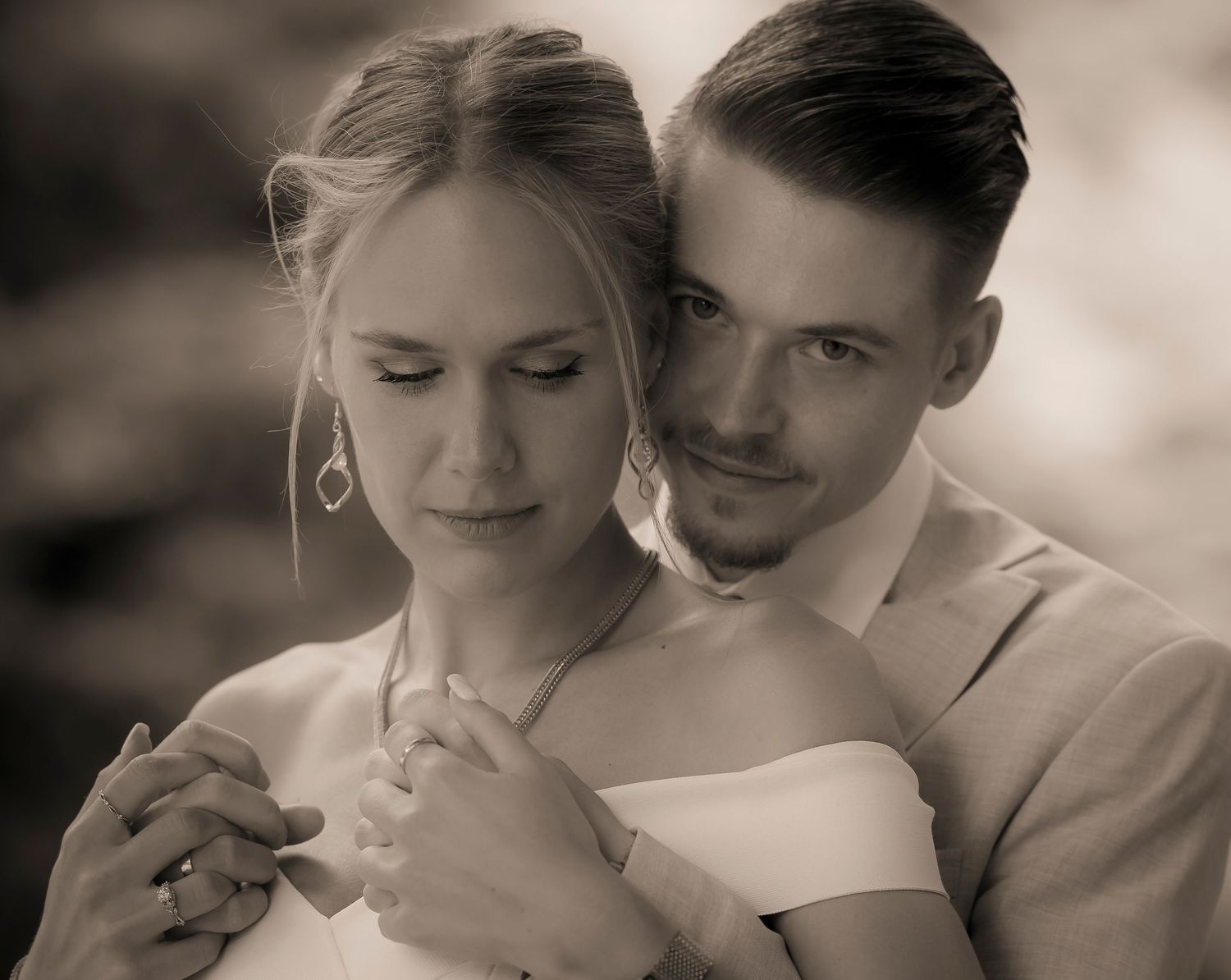 Romantic sepia portrait of bride and groom embracing tenderly outdoors.