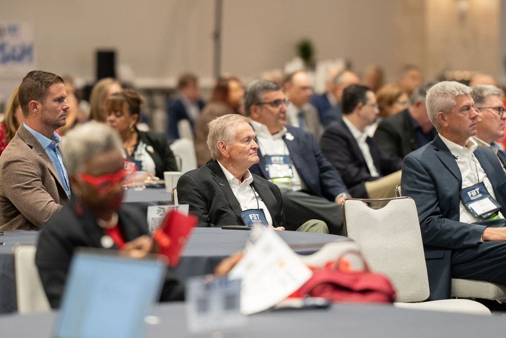 Business professionals attentively listening to a speaker at a corporate conference event in a large modern venue.
