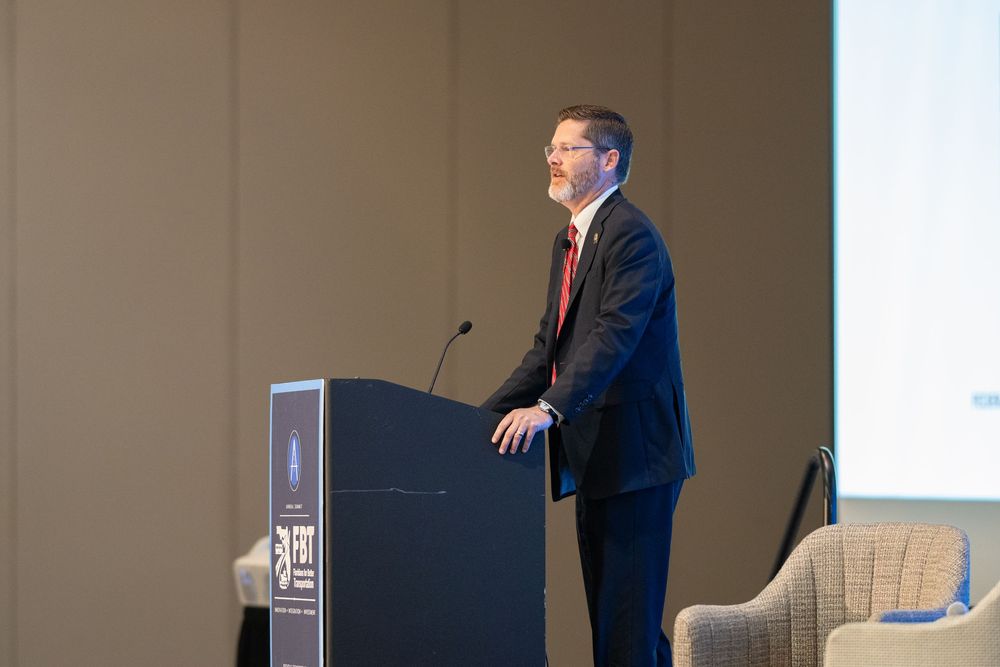 Professional male speaker presenting at a conference podium in a navy suit at a formal business event.