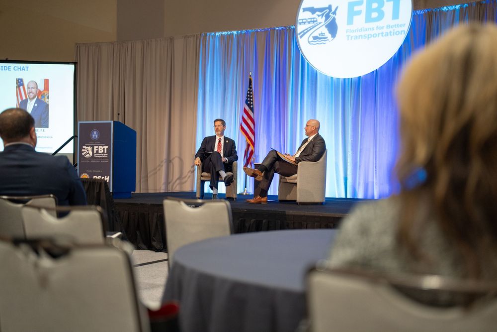 Two speakers on stage at FBT conference with American flag, audience seated in foreground at professional business event.