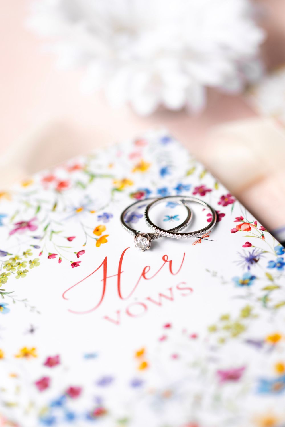 Close-up of diamond engagement rings resting on a floral Her Vows wedding booklet.