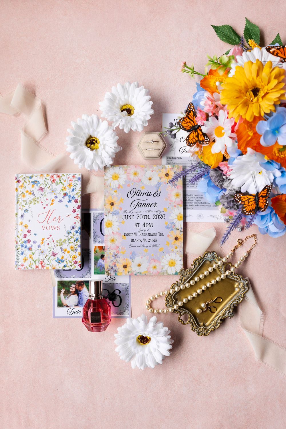 Colorful wedding flat lay with floral invitation, vow books, rings, and daisy bouquet.