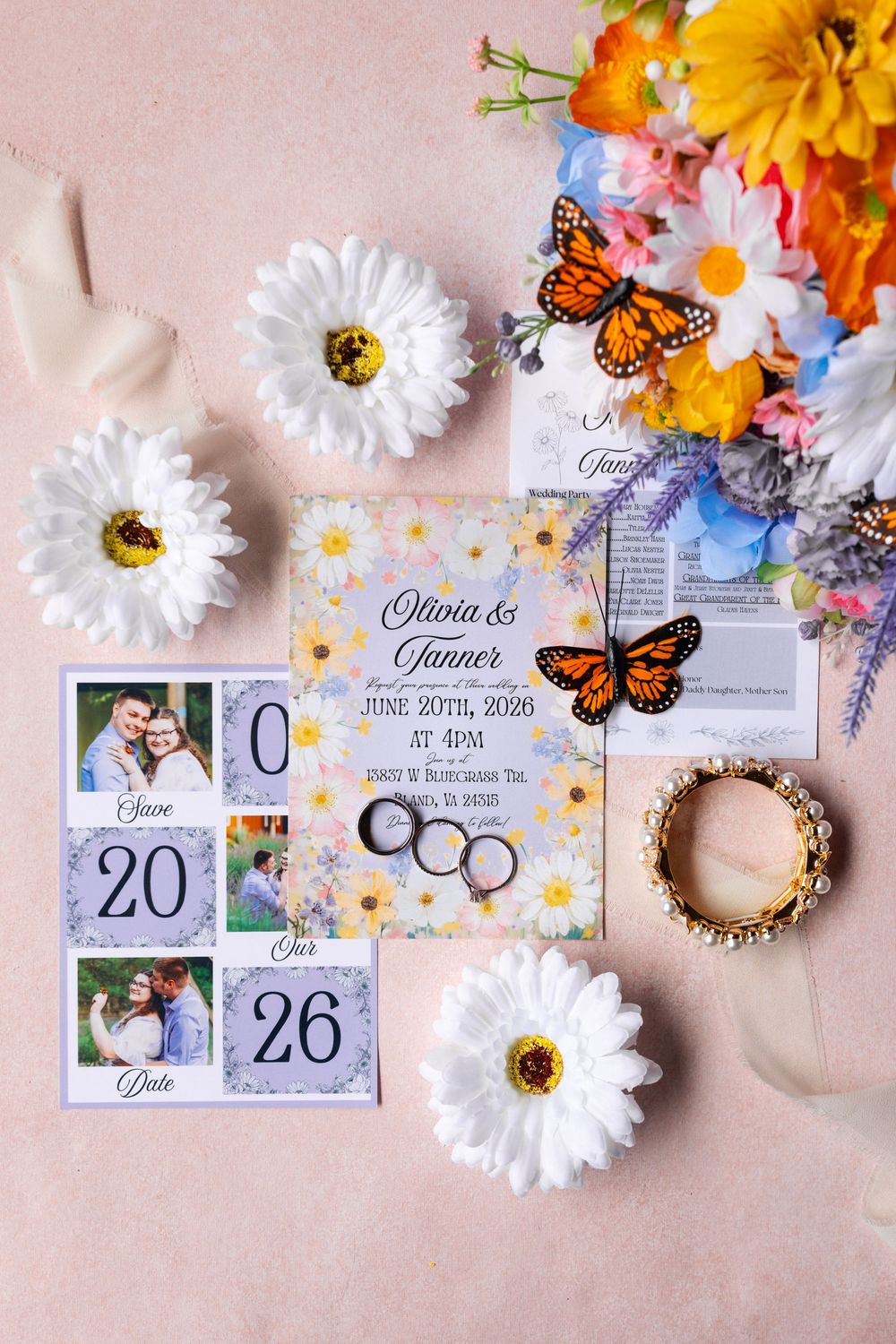 Wedding invitation suite for Olivia and Tanner with monarch butterflies, daisies, rings, save-the-date magnets, and floral arrangement.