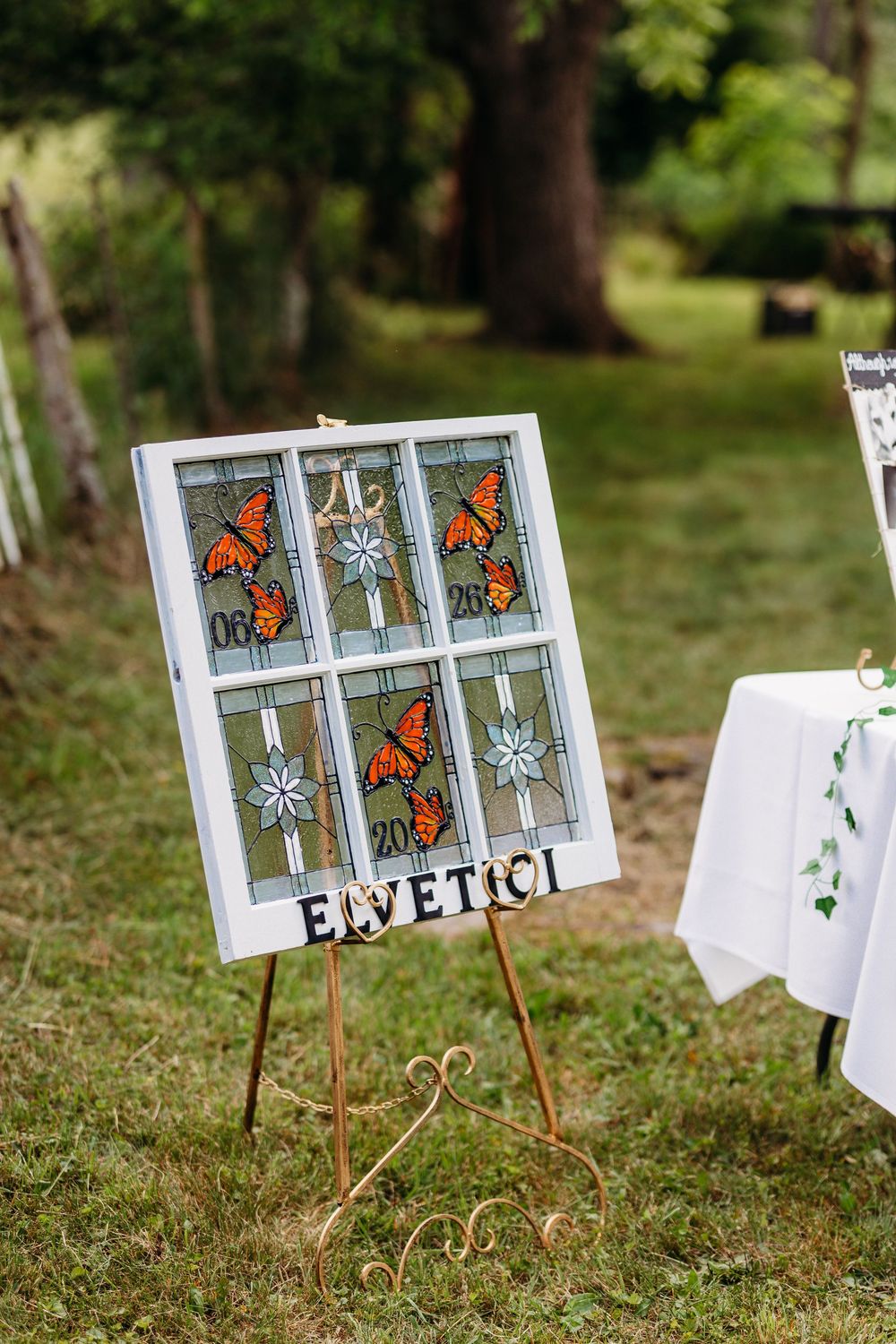 Stained glass window panel on easel with monarch butterflies displayed outdoors at a garden wedding event.