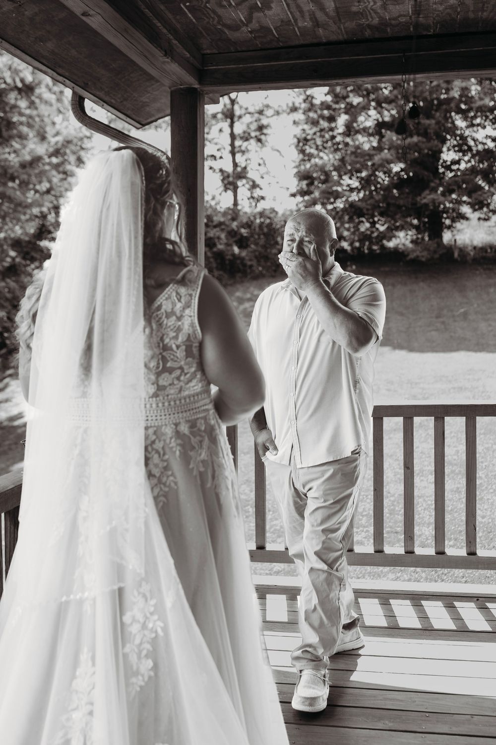 Emotional father seeing bride daughter in wedding dress for first time on porch, black and white photo.