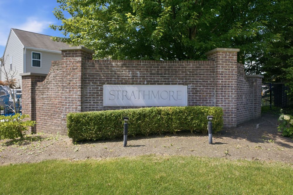 Brick entrance monument sign for Strathmore community surrounded by lush green landscaping and trees.