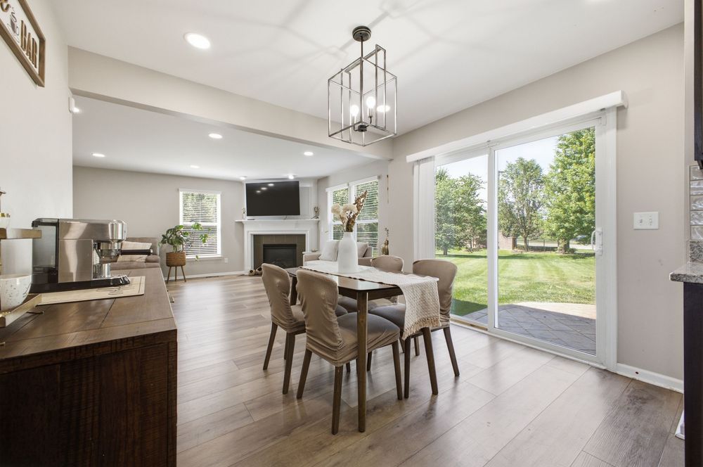 Bright open-concept dining room with hardwood floors, chandelier, fireplace, and sliding glass doors to backyard.