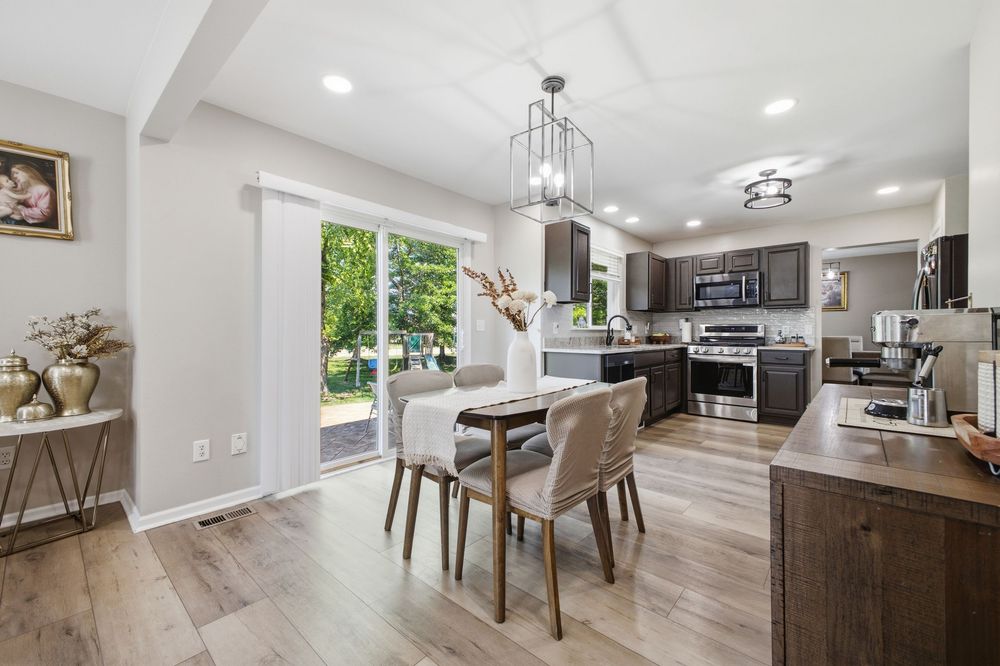 Modern open-concept kitchen and dining area with hardwood floors, dark cabinets, stainless appliances, and sliding glass doors.