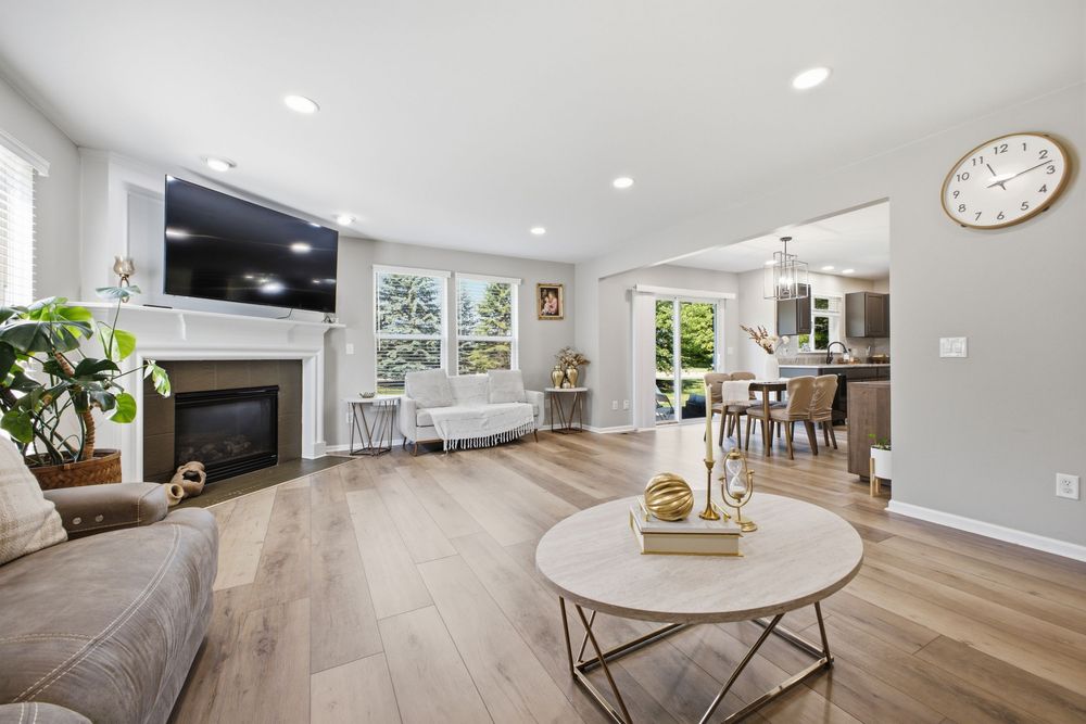 Bright living room with hardwood floors, white fireplace, wall-mounted TV, and open layout leading to dining area.