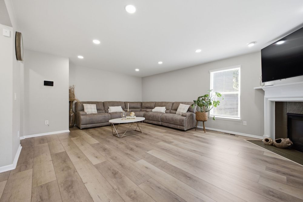 Spacious living room with light hardwood floors, gray sectional sofa, white fireplace, and wall-mounted TV.