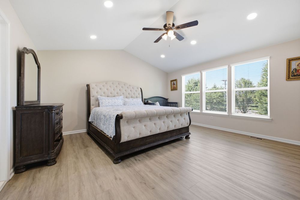 Bright master bedroom with vaulted ceiling, ceiling fan, hardwood floors, and elegant dark wood sleigh bed.