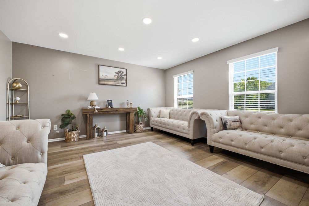 Bright living room with beige tufted sofas, hardwood floors, neutral walls, and a white area rug.