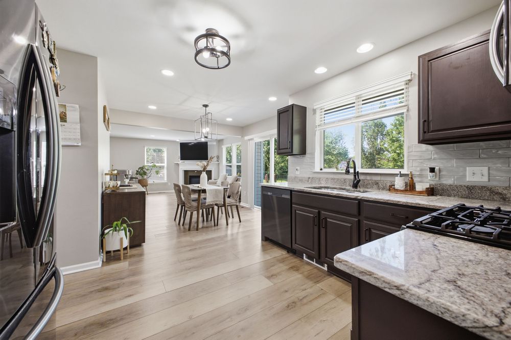 Modern kitchen with dark cabinets, granite countertops, stainless appliances, and open view to dining area with hardwood floors.