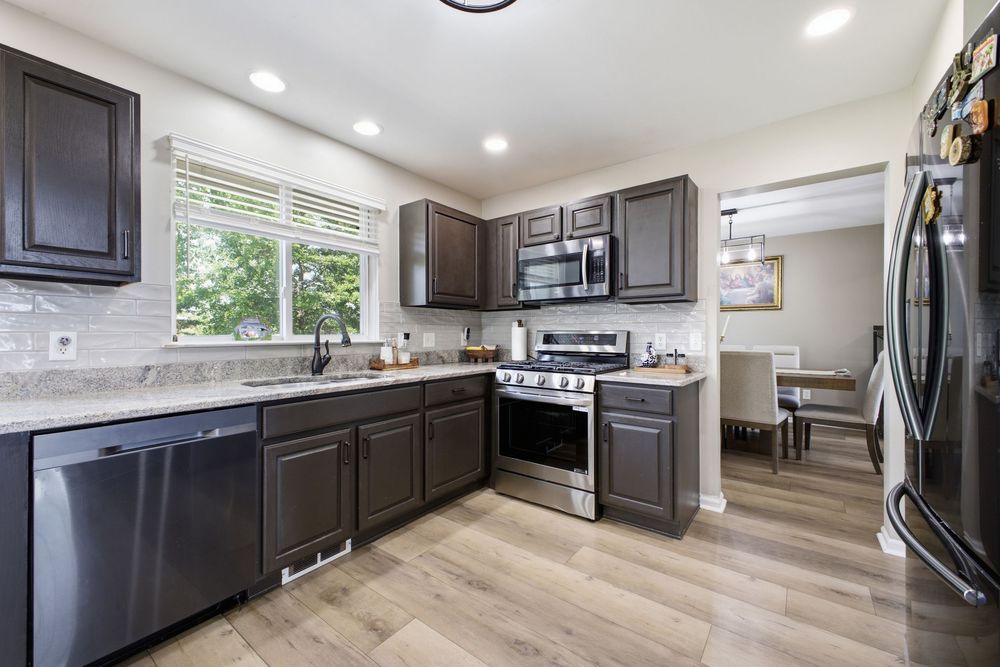 Modern kitchen with dark cabinets, stainless steel appliances, and light hardwood floors in a bright open layout.