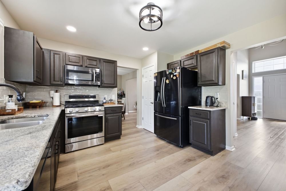 Modern kitchen with dark cabinets, stainless steel appliances, black refrigerator, granite countertops, and light hardwood floors.