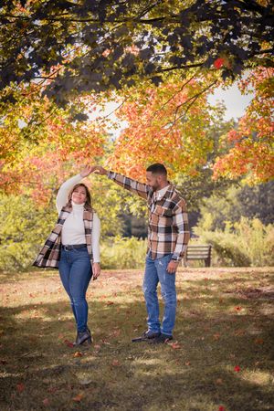 Couple in matching plaid shirts share a tender moment on a wooden bridge in autumn forest.