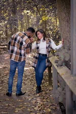 Romantic couple in matching plaid outfits sharing tender moment on autumn forest bridge.