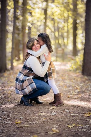 Mother and daughter sharing a warm hug on a forest path during autumn.