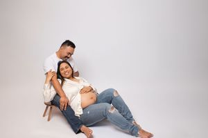 Expecting couple in white and jeans poses together on white background during maternity photoshoot.