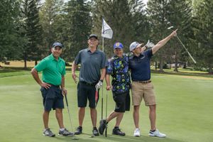 Four men smiling and posing together on a golf course green with a flag pin visible.