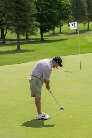 Male golfer putting on a lush green golf course on a sunny day near a flag marker.