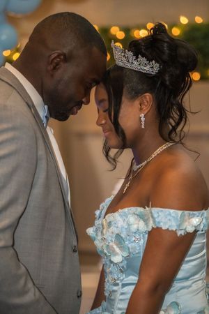 Tender moment between a man and young woman in blue quinceañera gown and tiara touching foreheads.