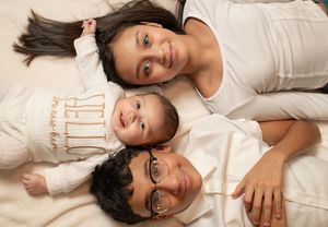 Three siblings lying together, two older children in white outfits with their baby brother between them.