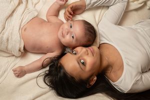 Mother and baby lying together on a soft cream blanket, sharing a tender moment in a warm newborn photography session.