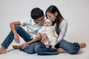 Young couple sitting on white floor holding their newborn baby, sharing a loving family portrait together.
