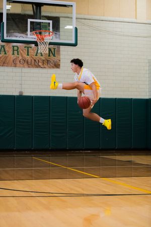 Athletic basketball player performs a dramatic mid-air jump near the hoop in a green and white gymnasium.
