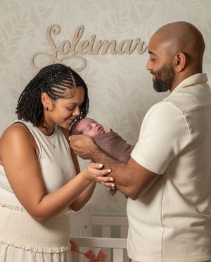 New parents admire their newborn baby in a nursery decorated with the name Soleimar on the wall.