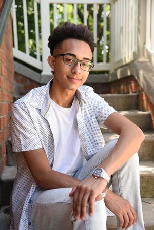 Stylish teenage boy in glasses and white shirt sitting on brick steps outdoors.