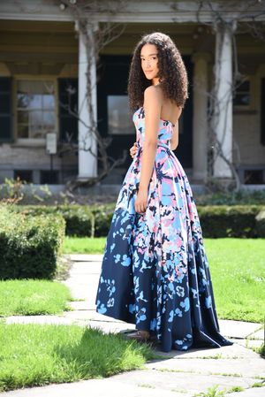 Young woman in a strapless navy floral ball gown posing outdoors in front of a historic home.