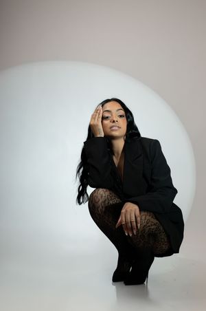 Woman in black blazer and leopard tights crouching in dramatic studio portrait with circular light.
