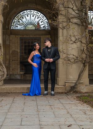 Prom couple posing in front of ornate stone building, woman in blue gown and man in black suit.