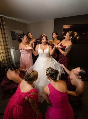 Bride in lace wedding gown surrounded by bridesmaids in pink and burgundy dresses.