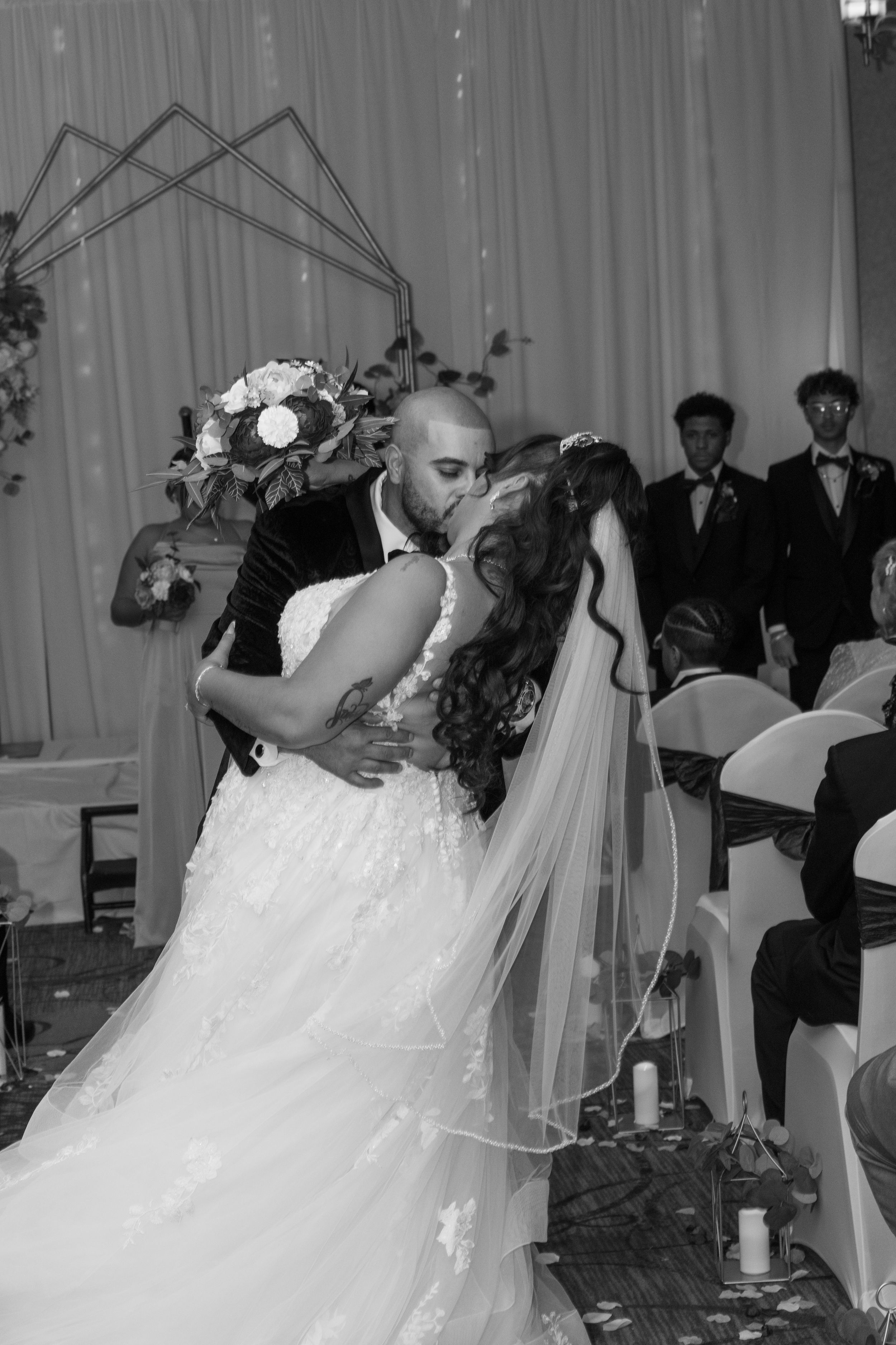 Black and white photo of bride and groom sharing first kiss at wedding ceremony altar.