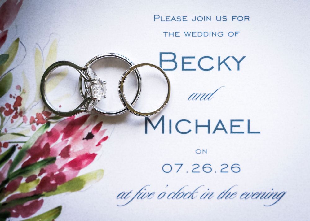 Wedding invitation for Becky and Michael on 07.26.26 at five o'clock, featuring two gold rings with a diamond engagement ring.
